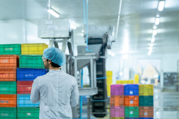 Naklejka premium A factory worker wearing protective gear, organizing colorful storage crates in a clean and modern industrial facility, showcasing efficiency, cleanliness, and organization in industrial operations.