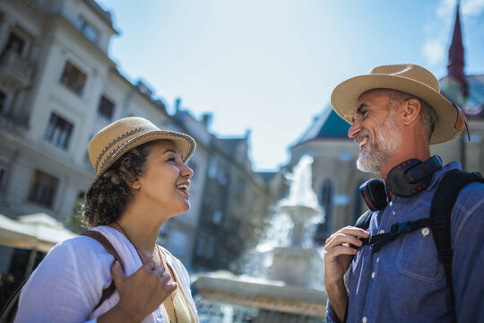 Senior couple of tourists stands happily in front of a stunning city fountain, surrounded by historic architecture