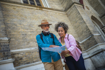 Portrait of happy senior couple tourists outdoors in historic town using map.
