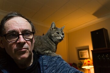 A mature man wearing glasses with cat on his shoulder