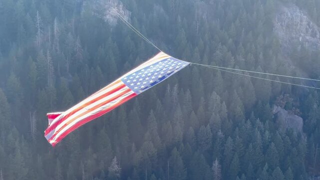 Largest US American flag floating and waving majestically in the breeze over a forested canyon in Ogden Utah -hike to the Major