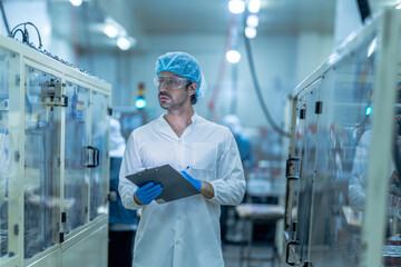 A food processing supervisor wearing protective gear and holding a clipboard, inspecting operations between machinery in a factory, emphasizing hygiene, safety, and quality control in production