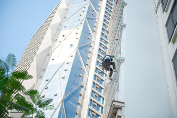 Professional Asian industrial climber worker at height cleaning outside high rise building tower in...