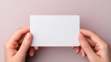 A pair of hands holds a blank white card against a soft, muted background, suggesting potential for writing or design.