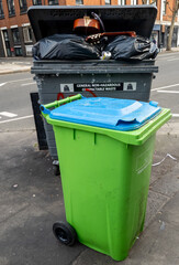 Garbage bins of a restaurant out on the street awaiting collection, with the black bin for general waste and the green one for recycling.