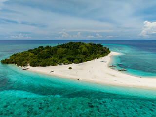 Flying over the white beach with turquoise water in Mantigue Island. Blue sky and clouds. Camiguin, Philippines.