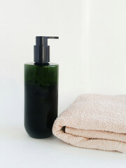 A dark green bottle with a dispenser and a pink terry towel are on the table. Lotion for dry hair care. Shower gel for delicate skin. Hypoallergenic shower gel, shampoo.
