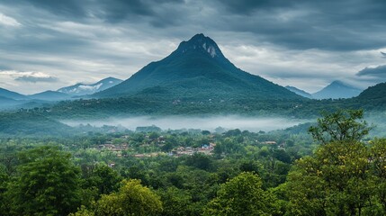 Fototapeta premium Majestic mountain landscape shrouded in mist with lush green foreground and dramatic cloudy sky in serene natural setting