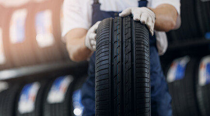 Closeup mechanic holding new tire at store warehouse with sunlight. Concept banner replacement of winter and summer tyres © Parilov