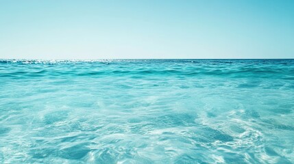 Obraz premium Vibrant turquoise ocean water with gentle waves reflecting sunlight against a serene clear sky in a minimalist composition