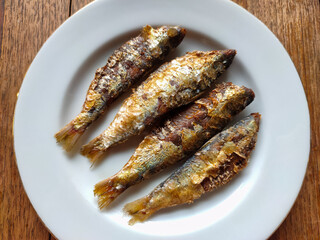 Close up of salted fish on a white plate on a wooden table. Salted fish is a food made from fish meat preserved with salt.