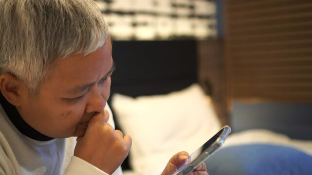 Senior smart chatting in Video call to family in New normal life in bedroom, Reading social media internet and typing text or shopping online with smartphone mobile.