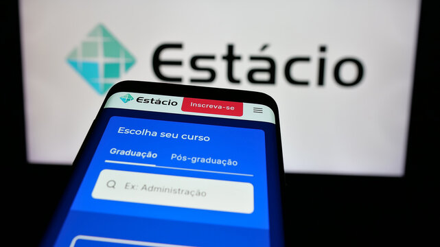 Stuttgart, Germany - 12-16-2024: Mobile phone with website of Brazilian educational company Estacio SA on screen in front of business logo. Focus on top-left zof phone display.