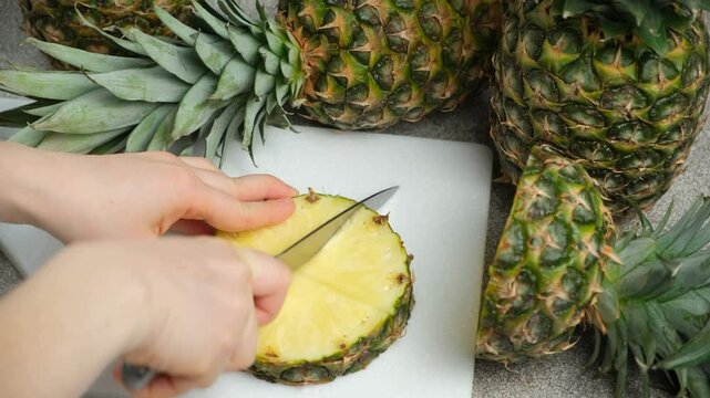 Hands cutting fresh pineapple fruit into pieces.