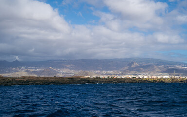 Coastal view from the waters near Tenerife, featuring dramatic rocky cliffs to the right and a...