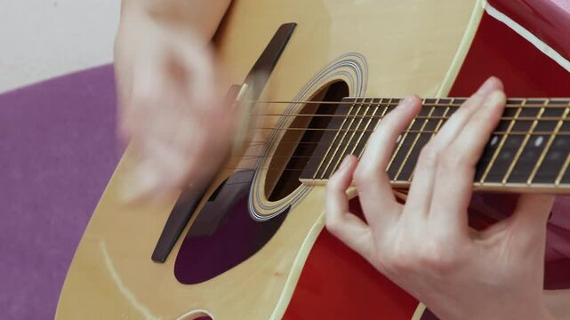 Close-up view of female guitarist is performing captivating solo, deftly manipulating fingers over frets and neck of acoustic guitar. This performance, executed in strumming style with guitar pick
