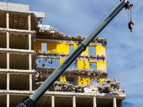 arm of a mobile crane at a partially demolished building showing exposed concrete floors, yellow structural columns, and tangled reba