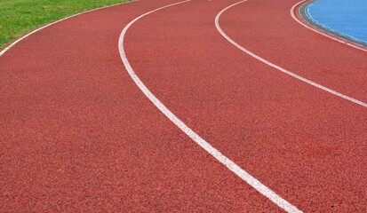 red running track curve with white lines and green grass in right side