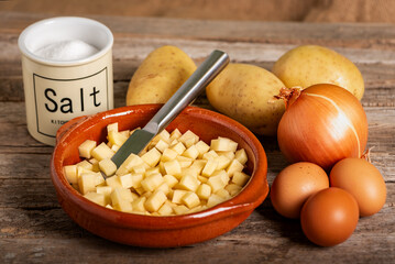 Ingredients to cook a Spanish potato omelette: diced potatoes, onion, eggs, and salt, on a rustic wooden table, close-up.
