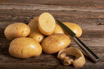 Potatoes for consumption on a rustic wooden table, alongside a potato cut in half and a knife,...