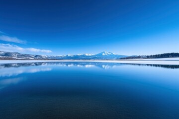 Fototapeta premium Photograph of Mount Fuji in Japan with a clear blue sky and a calm lake, the reflection on the water surface creating a geometric abstract design.