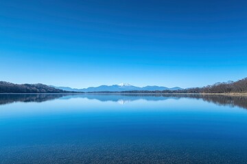 Obraz premium Photograph of Mount Fuji in Japan with a clear blue sky and a calm lake, the reflection on the water surface creating a geometric abstract design.