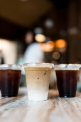 Close up view a glass of ice latte placed on the center between ice black coffee, desk blurred background, drink beverage