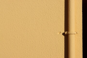 Light yellow concrete wall with pits and roughness, vertical pipe and small fitting with rivets. High resolution with large copy space and detail