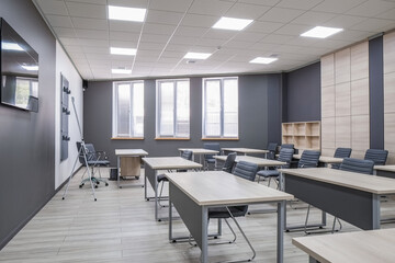 Modern classroom or office space with desks and chairs, a large wall-mounted TV, a whiteboard, and large windows providing natural light