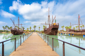 Replica ships at Caravel Dock Museum. Wooden ships with masts and sails, docked in calm waters....