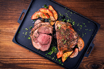 Traditional lamb leg roll roast with herbs and quince fruit as top view on a cast iron tray