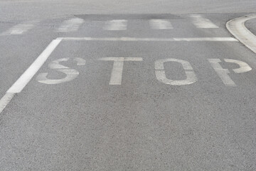 The word STOP painted in white on gray asphalt at a road intersection, indicating a mandatory stop for vehicles
