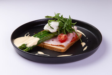 Sandwich with ham and asparagus in a plate on a light background.