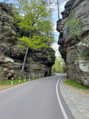 Asphalt road between two rocks in the forest in the Mullerthal region, Luxembourg.