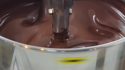 Closeup of melted chocolate being turned in a large stainless steel mixing machine in an artisanal chocolate making factory