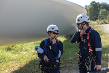 Inspection engineers a rotor blade of a wind turbine. Professional Man Maintenance engineers working in wind turbine farm. Engineer Man standing among Wind Energy Turbine.