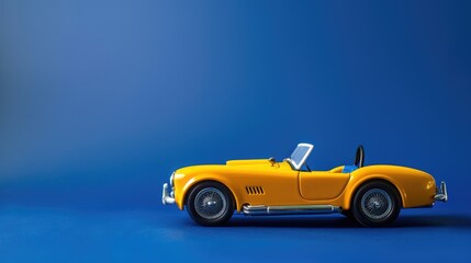 Fototapeta premium A vintage yellow toy car set against a deep royal blue background, evoking a sense of nostalgia with a bold twist.