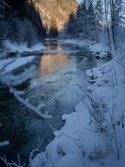 Sunlit River Cutting Through A Frosty Winter Forest: A Tranquil Harmony Of Snow, Ice, And Golden Light