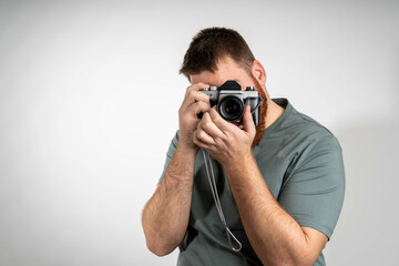 Focused young man holding a camera against a grey background, capturing a moment with attention and precision.