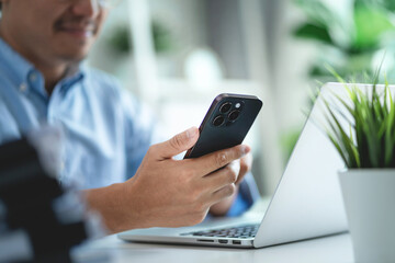 A man is holding a cell phone and smiling. He is in front of a laptop computer.