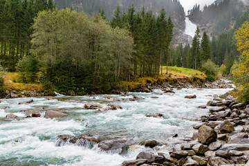 Alpine river flowing through forest valley near Krimml Waterfalls in the Austrian Alps on a cloudy day