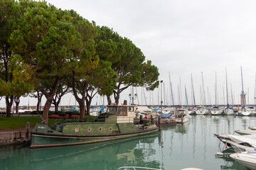 Fototapeta premium A scene in Desenzano del Garda's port, with a focus on a vintage work boat and numerous sailboats in the background