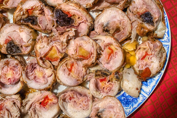 Top view of sliced stuffed chicken rolls with ham, cheese, bell pepper, and plum, on a white plate with blue floral pattern