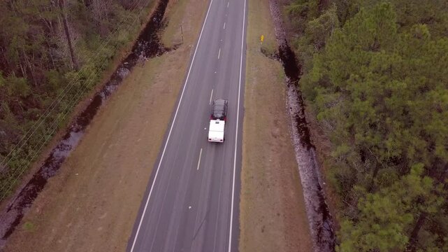 Aerial view of car pulling teardrop camper down empty highway.