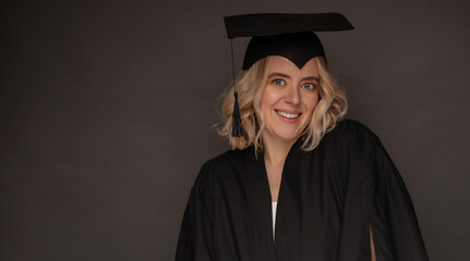 Portrait of a smiling female graduate in a black cap and gown against a neutral background, celebrating academic achievement and success. Ideal for education, graduation, and achievement concepts.