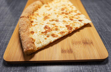 A close-up of three thin slices of pizza with four types of cheese lying on a rectangular bamboo cutting board.
