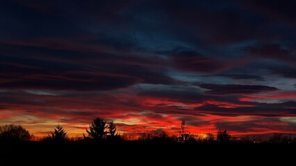 Deep blue sky with vivid crimson and purple streaks, highlighting the contrast between light and darkness.