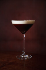 A dark espresso martini served in an elegant cocktail glass, with a creamy foam topping, set against a rich, dark background