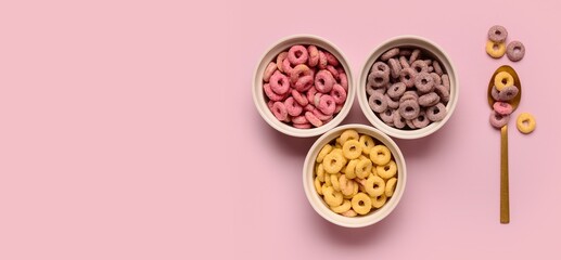 Bowls of colorful sweet cereal rings and spoon on pink background with space for text, top view