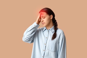 Young woman feeling pain in head on beige background